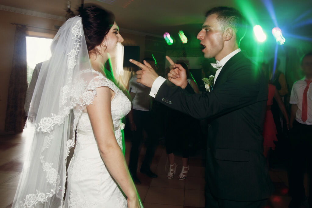 Bride and groom laughing together on the dance floor under colorful reception lights