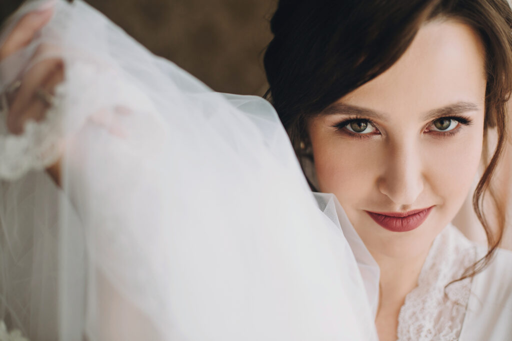Close-up portrait of a bride holding her veil, looking directly at the camera