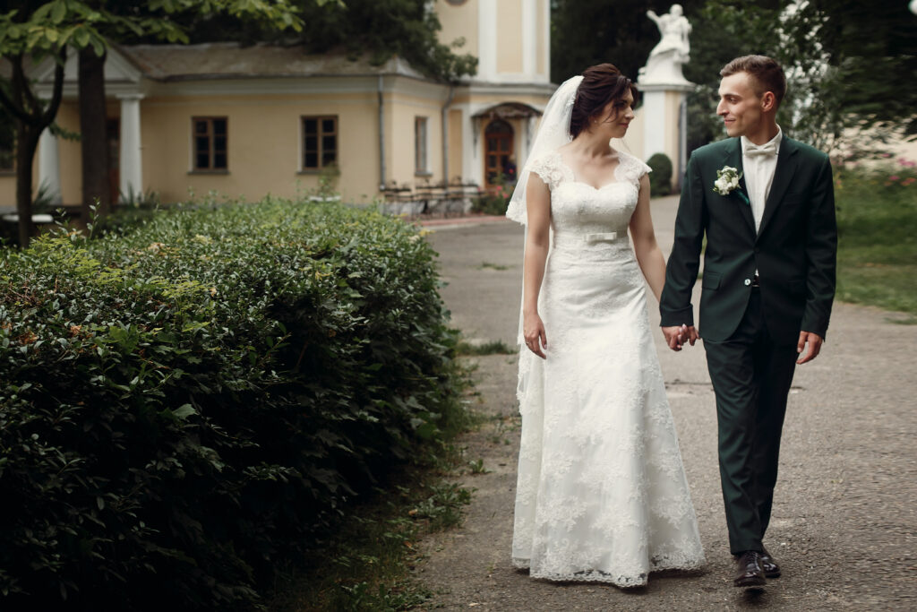 Bride and groom holding hands, walking together on a garden path outdoors