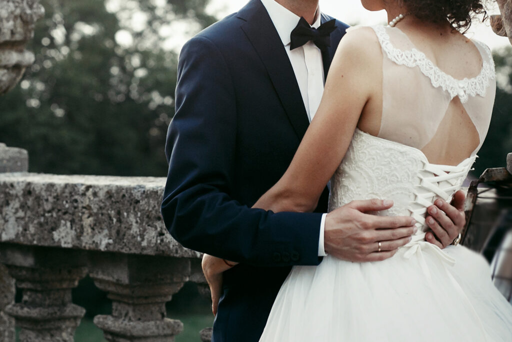 Close-up of groom's arm around bride's waist, showing her lace corset-back wedding dress